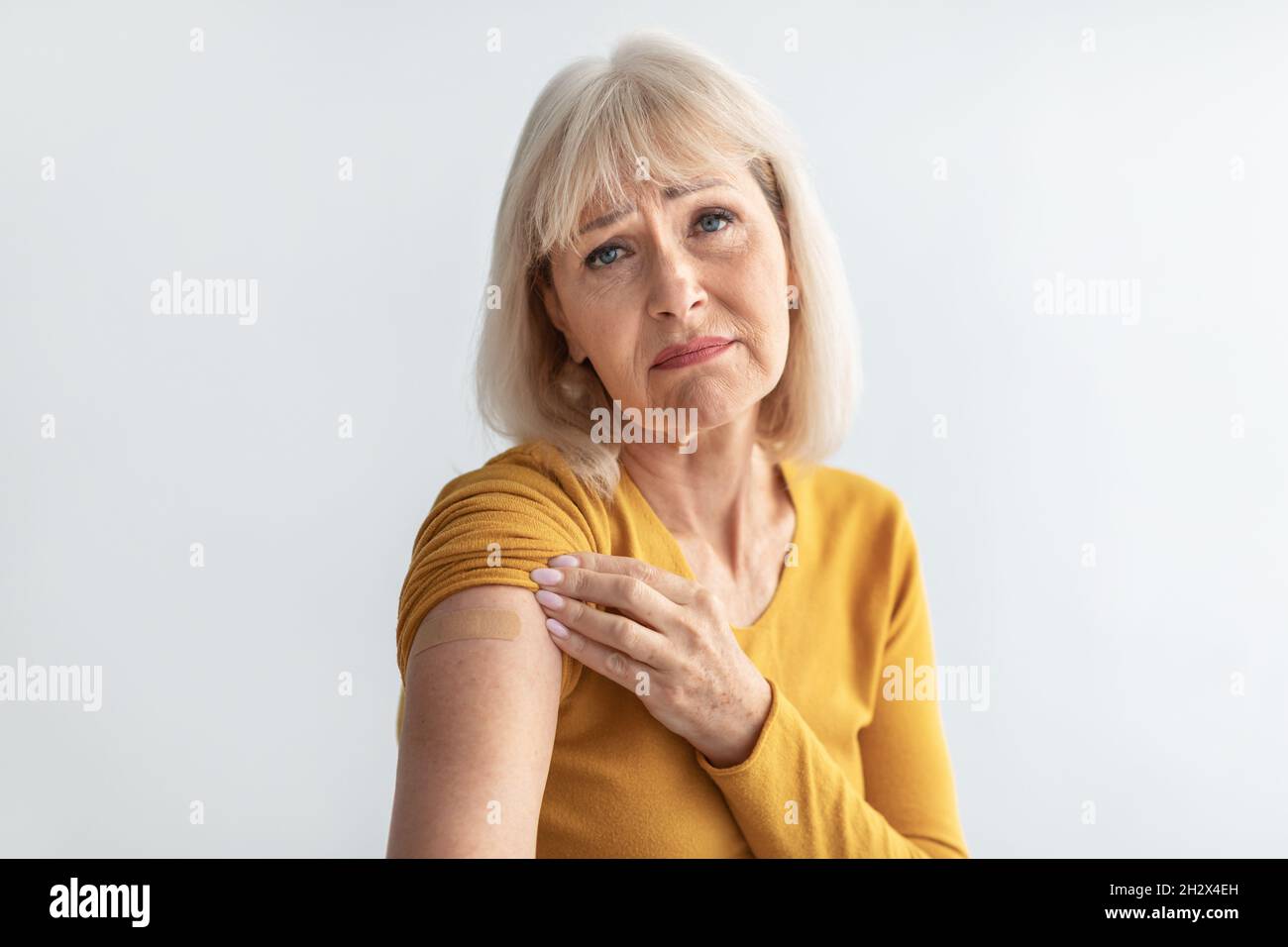Femme âgée malheureuse montrant bras vacciné avec plâtre, fond gris Banque D'Images