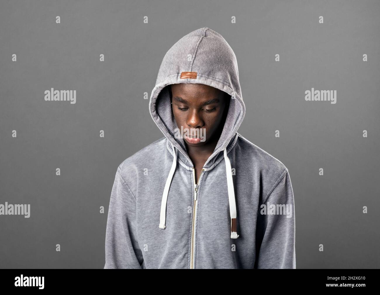 Jeune homme noir portant un sweat à capuche gris regardant vers le bas avec  une expression sombre sérieuse dans un gros plan tête et épaules portrait  sur gris Photo Stock - Alamy
