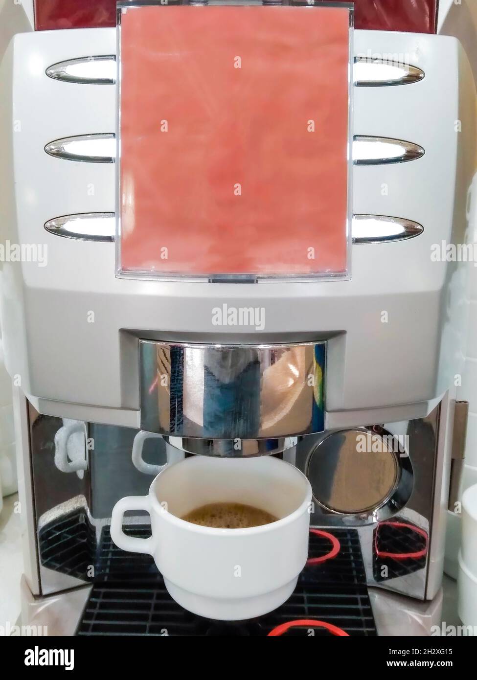 L'avant d'une machine à café avec des boutons de choix pour le libre-service et une tasse de café prête à boire Banque D'Images