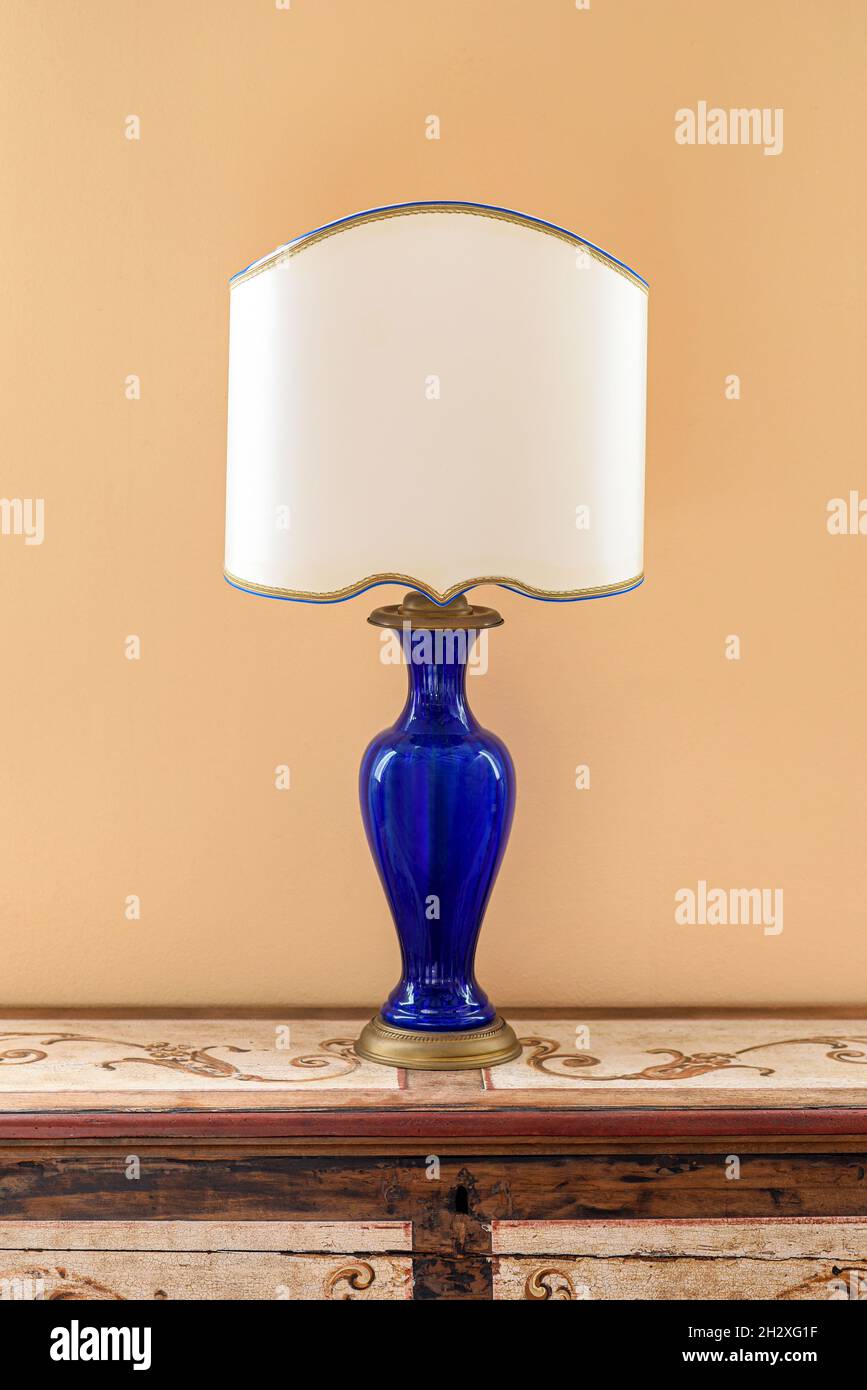 Lampe des années 50 avec support en verre bleu et abat-jour blanc placé sur une commode en bois contre un mur jaune dans la pièce Banque D'Images