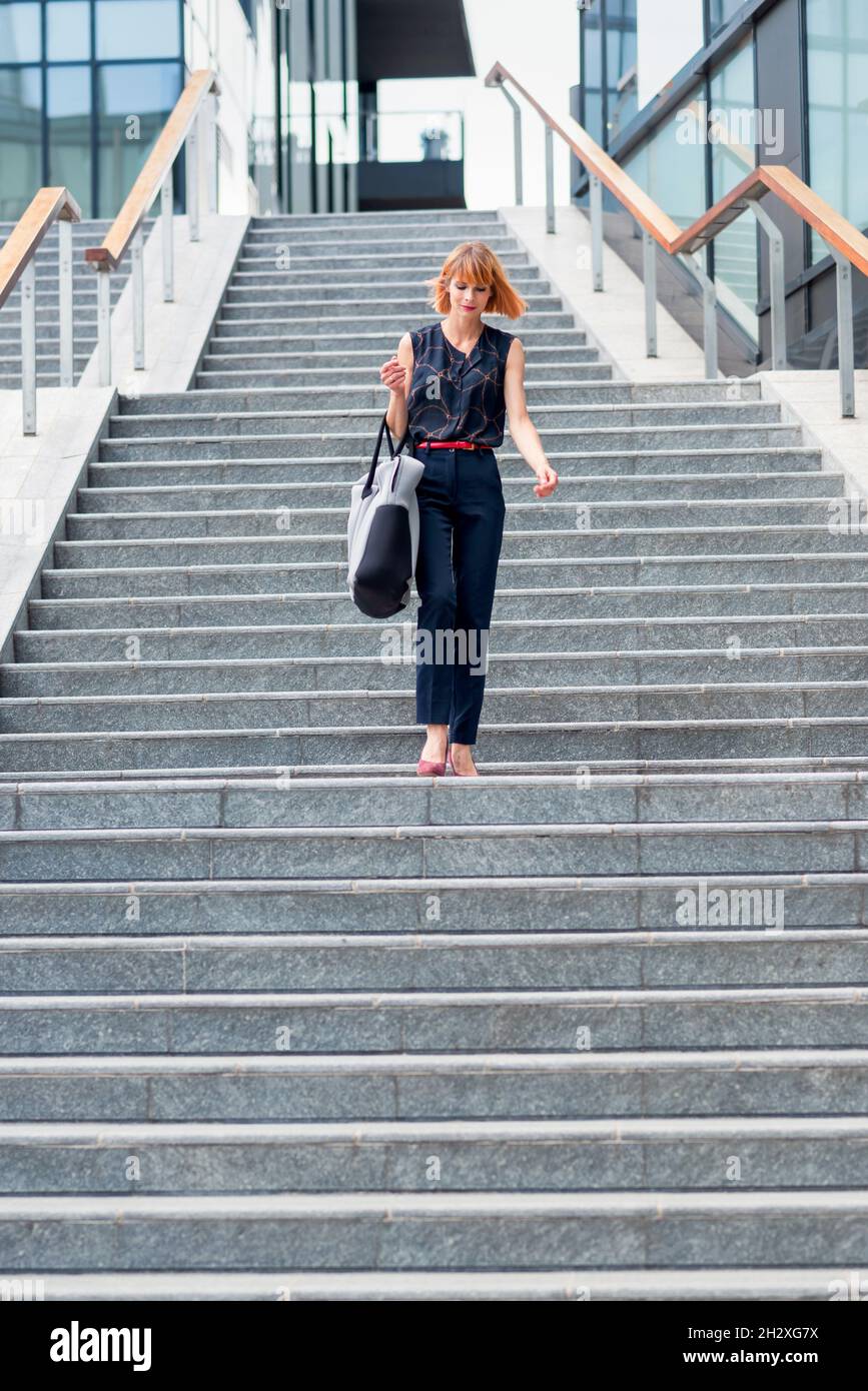 De dessous de corps de jeune femme moderne dans une tenue élégante avec sac marchant dans l'escalier dans la ville en été Banque D'Images