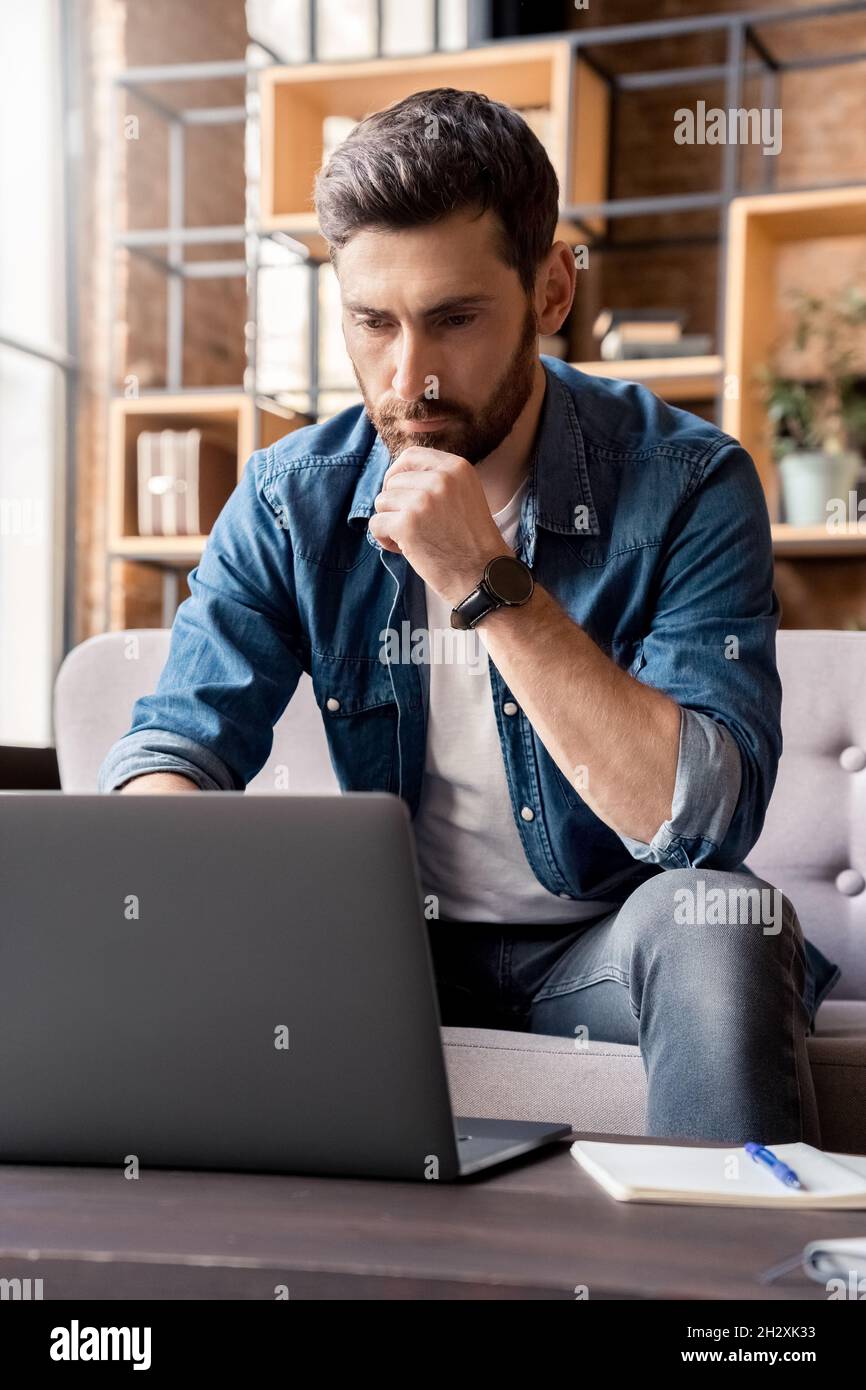 Homme concentré lisant des informations et vérifiant des données travaillant en ligne sur ordinateur portable Banque D'Images