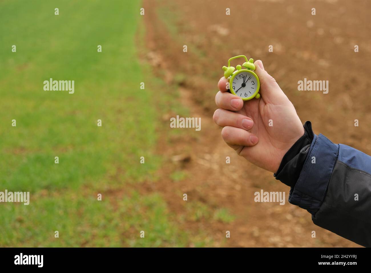 Temps d'ensemencement du printemps.Temps d'ensemencement..saison de travail dans les champs- Agriculture et agriculture.Le champ est vert et labouré et une main d'homme avec un réveil vert Banque D'Images