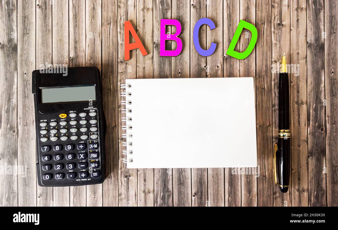 les lettres de l'alphabet de lettres de couleur bois se trouvent sur une table marron, à côté d'un bloc-notes pour l'écriture, d'une calculatrice et d'un stylo Banque D'Images