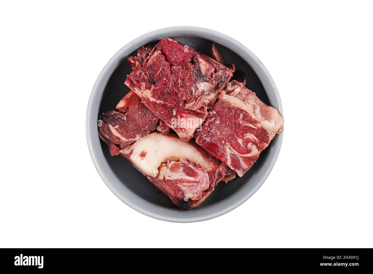 Bol pour chien avec gros morceaux rouges de viande avec graisse utilisé pour une alimentation biologiquement appropriée sur fond blanc Banque D'Images
