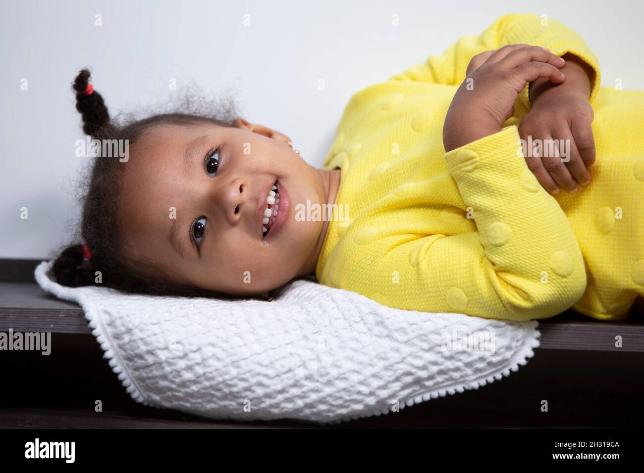 Une petite fille afro-américaine en robe jaune se cache et sourit. Banque D'Images