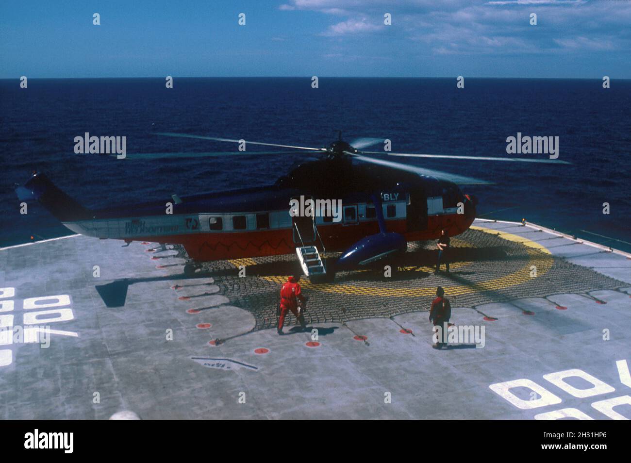 Homme portant une combinaison de survie à pied jusqu'à l'hélicoptère, engin de forage semi-submersible offshore SEDCO 700, puits de forage dans la mer celtique en 1987, au large de Cork Banque D'Images