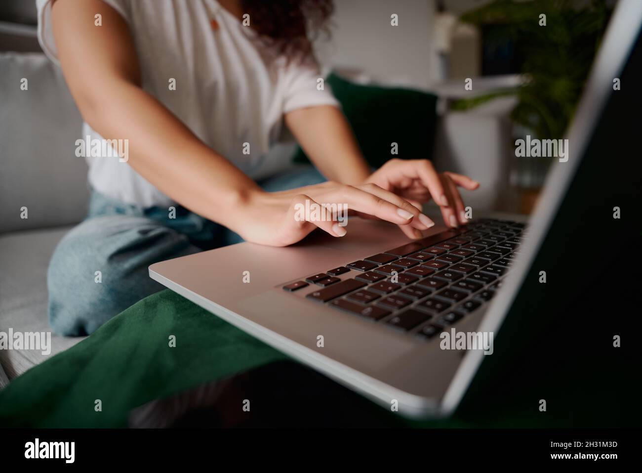 Gros plan des mains d'une femme multi-ethnique dactylographiant sur un ordinateur portable tout en étant assise sur le canapé Banque D'Images