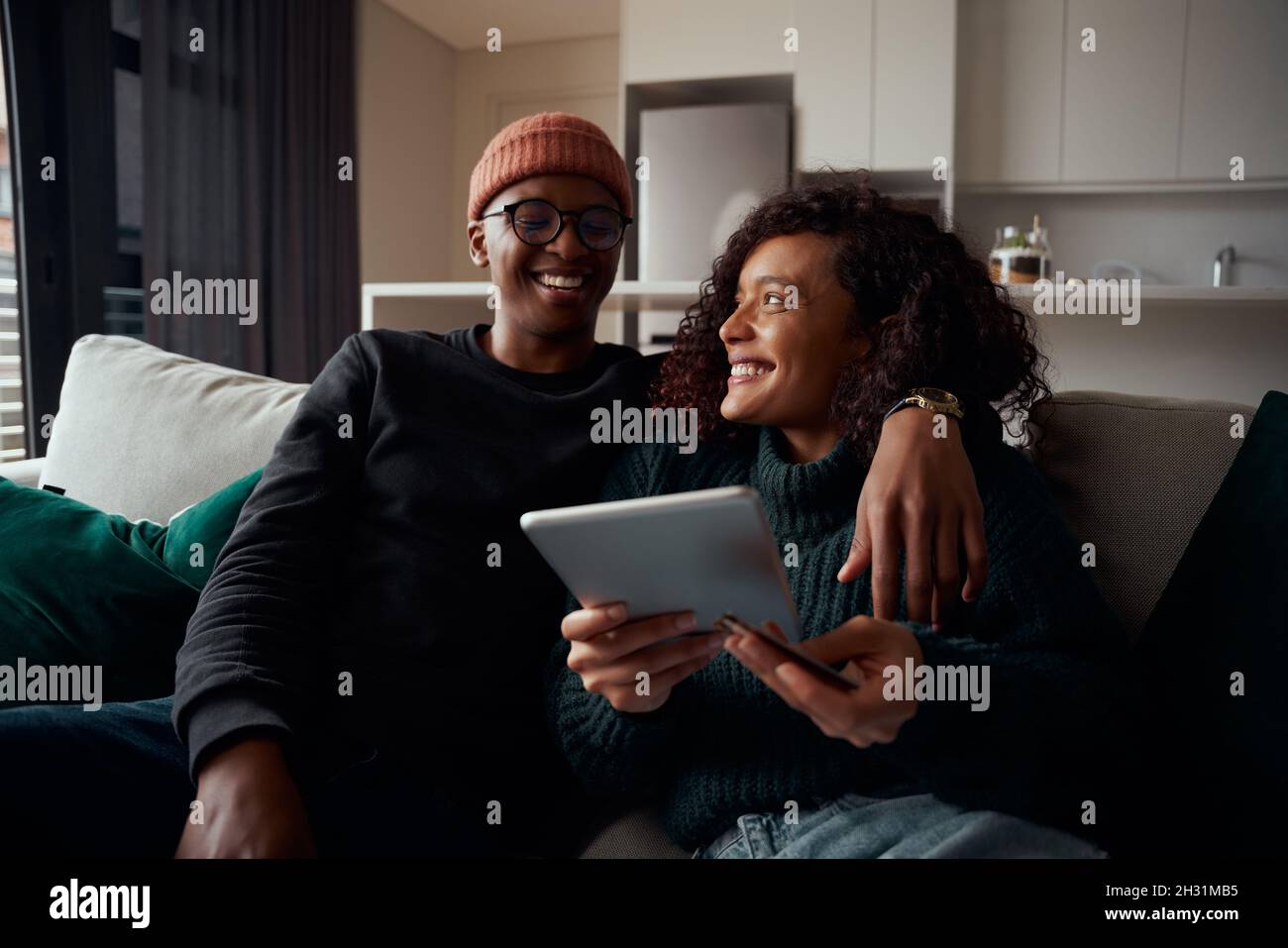 Couple adulte heureux, multi-ethnique, paiement en ligne sur tablette canapé dans l'appartement moderne Banque D'Images