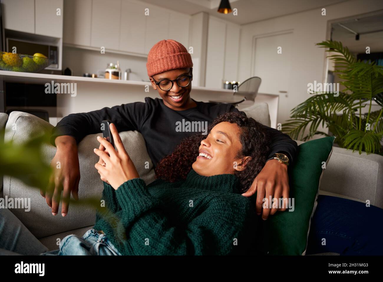 Couple multiethnique se regardant les uns les autres, en riant au sujet du texte sur le téléphone.Sur un canapé dans un appartement moderne Banque D'Images