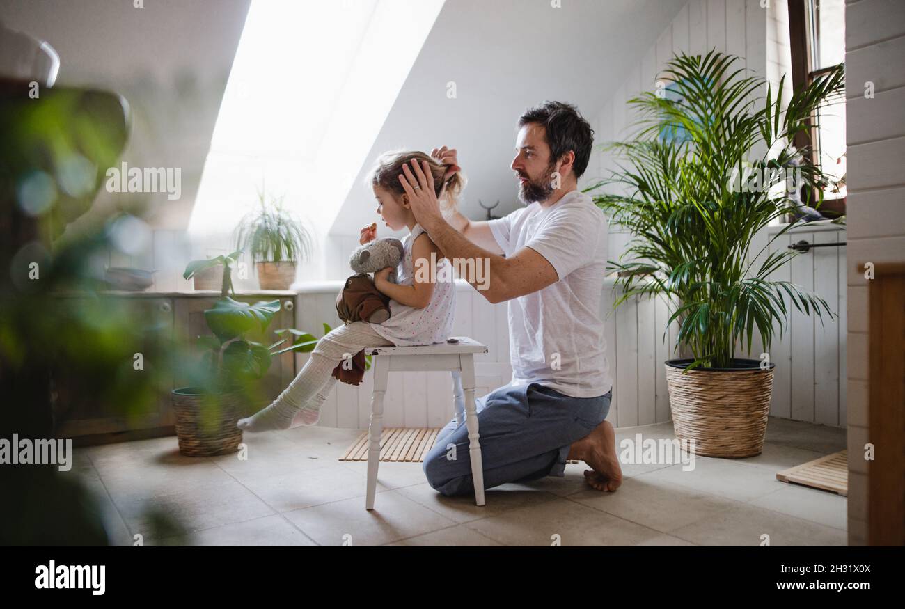 Père mature avec petite fille à l'intérieur dans la salle de bains à la maison, peignant les cheveux. Banque D'Images