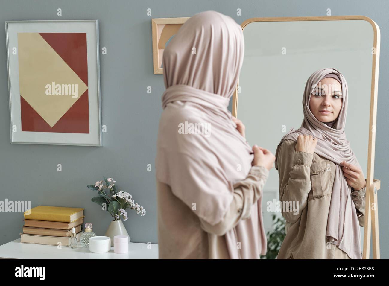 Jeune femme musulmane en hijab regardant dans un grand miroir tout en s'habillée pour le travail le matin Banque D'Images