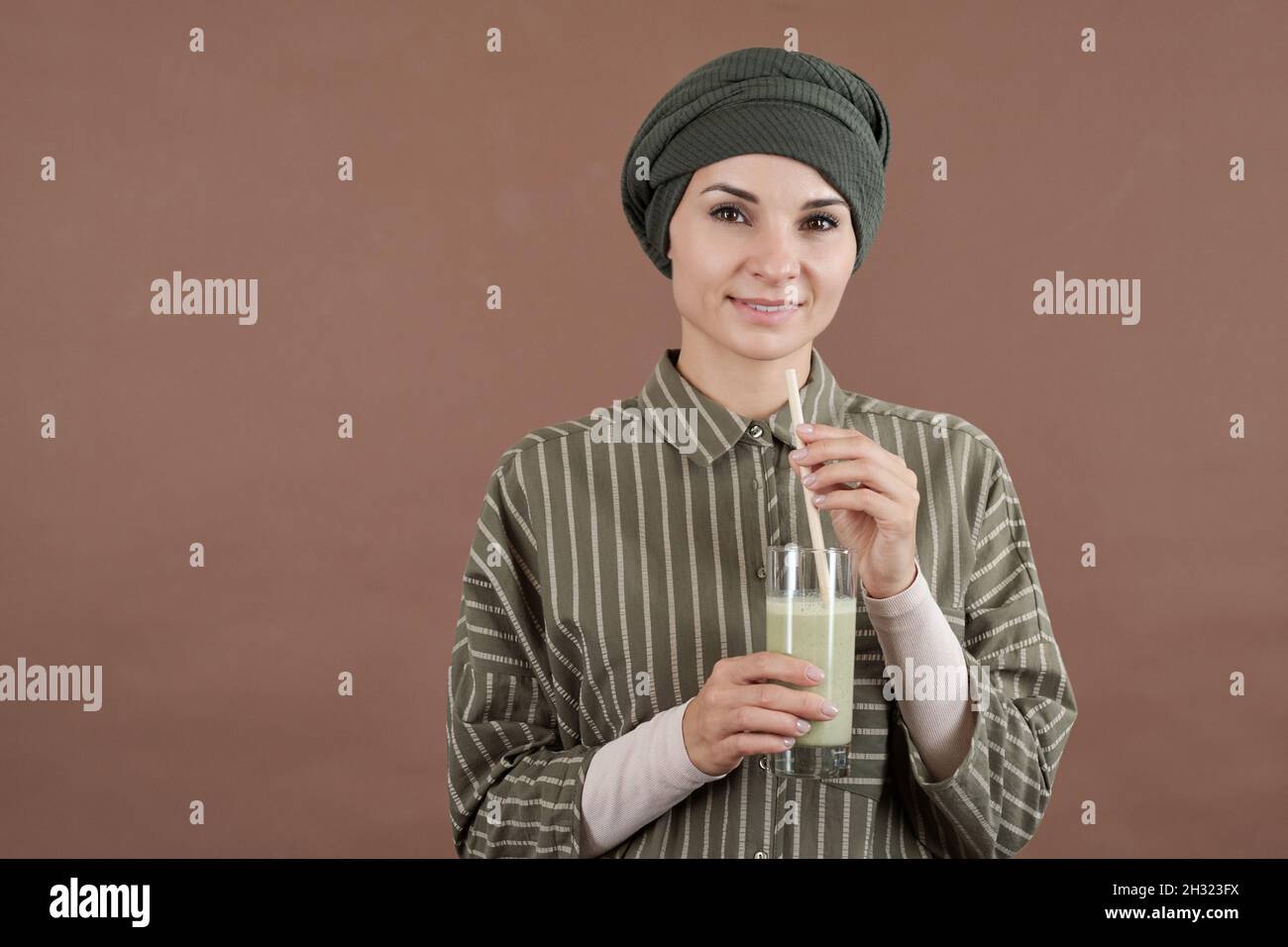 Jeune femme souriante avec un verre de cocktail de lait ou smoothie debout devant l'appareil photo sur fond marron Banque D'Images