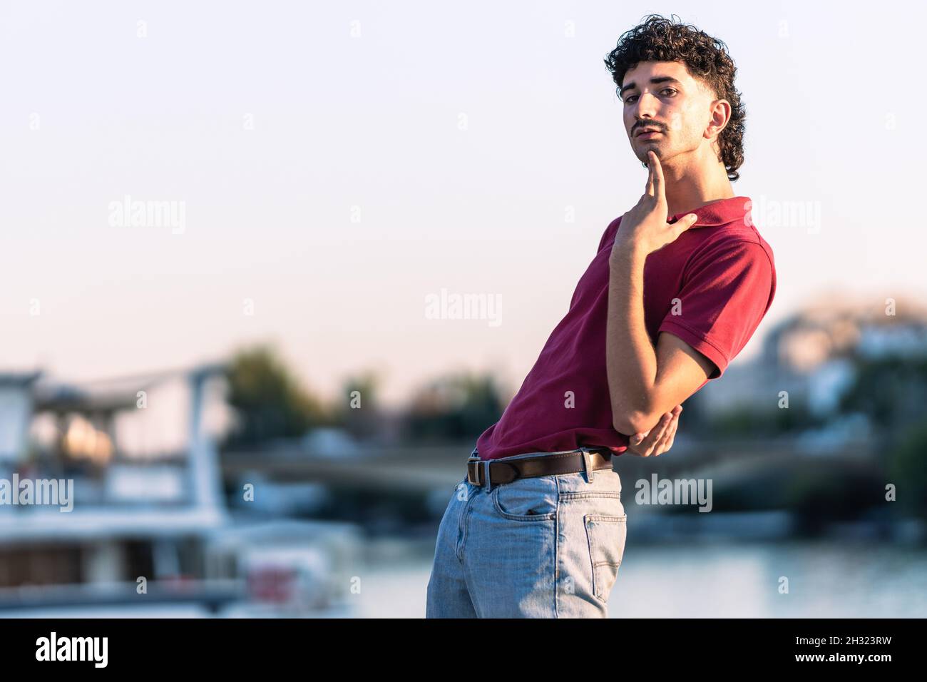 Portrait d'un jeune homme efféminé avec un regard moderne à côté d'une rivière urbaine Banque D'Images