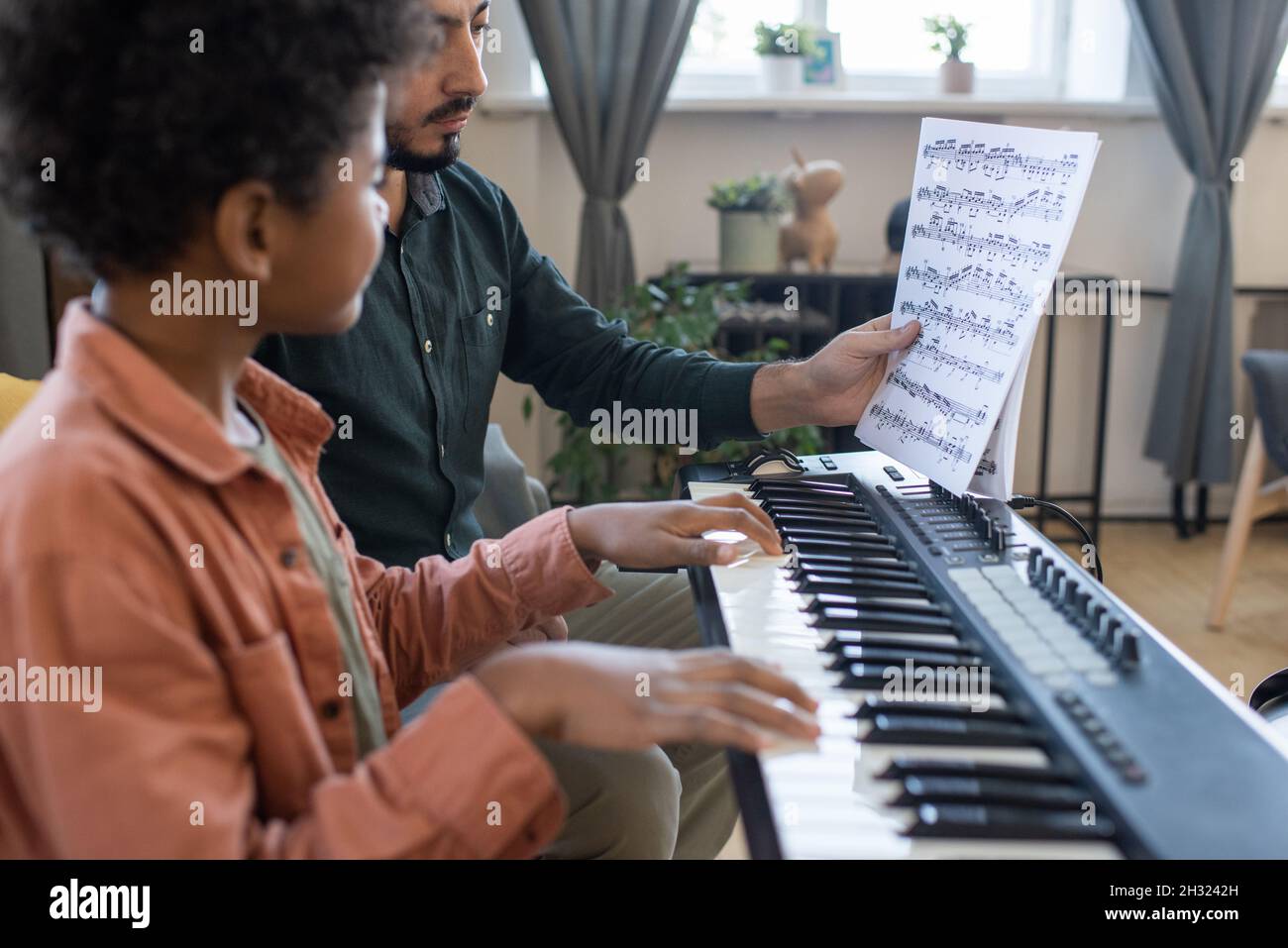 Professeur de musique montrant le petit papier d'un élève avec des notes tout en étant assis au clavier de piano à la leçon Banque D'Images