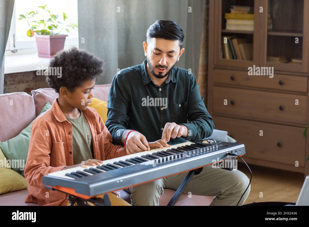 Jeune professeur de musique consultant petit écolier sur le jeu de clavier de piano à la leçon à la maison Banque D'Images