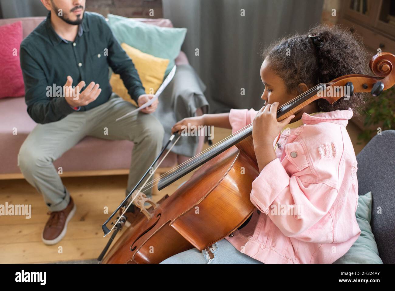 Petite fille biraciale mignonne à travers les cordes de violoncelle, assis devant son professeur de musique Banque D'Images
