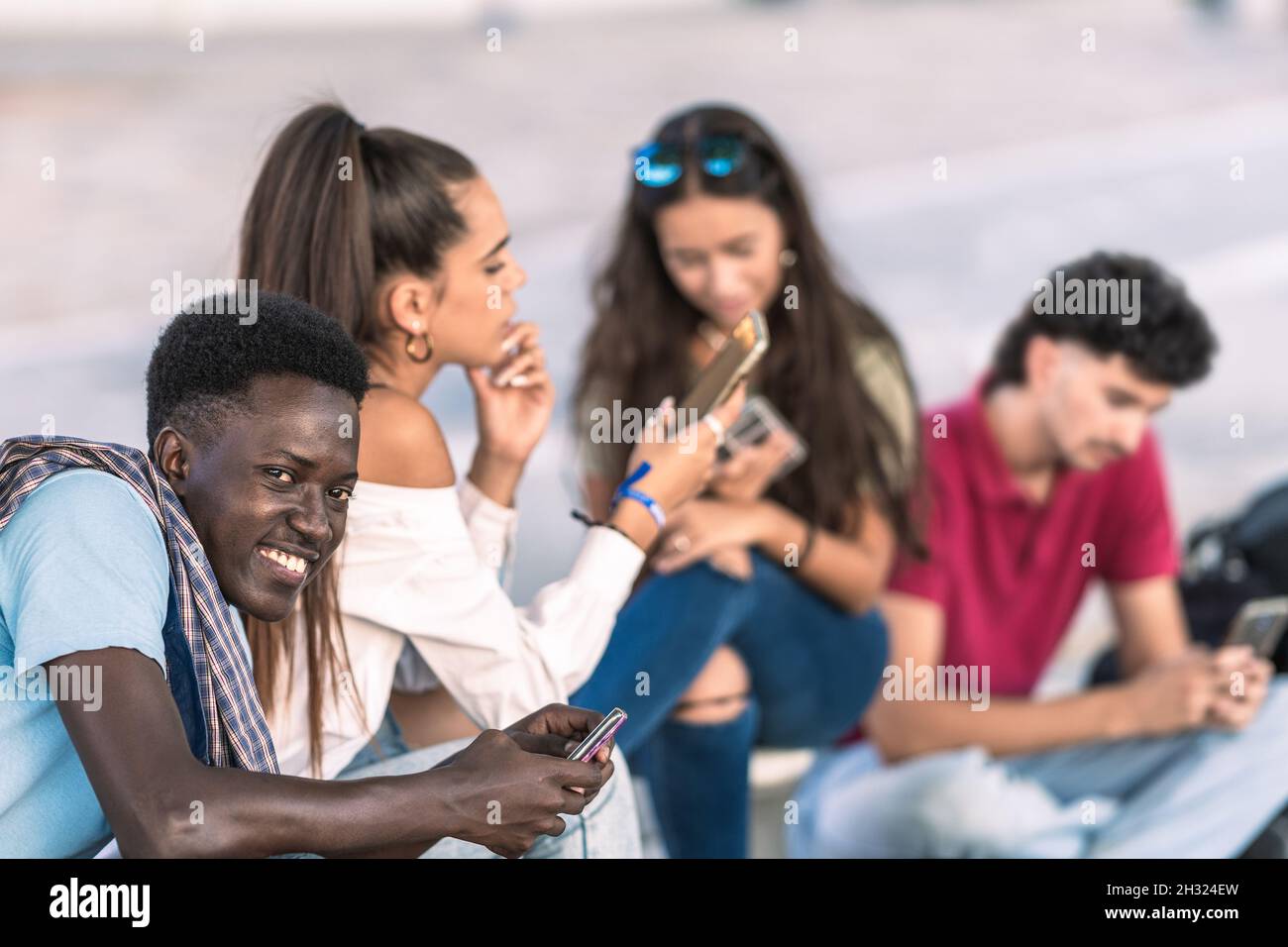 Afro homme assis à côté de divers groupes d'amis utilisant le mobile Banque D'Images