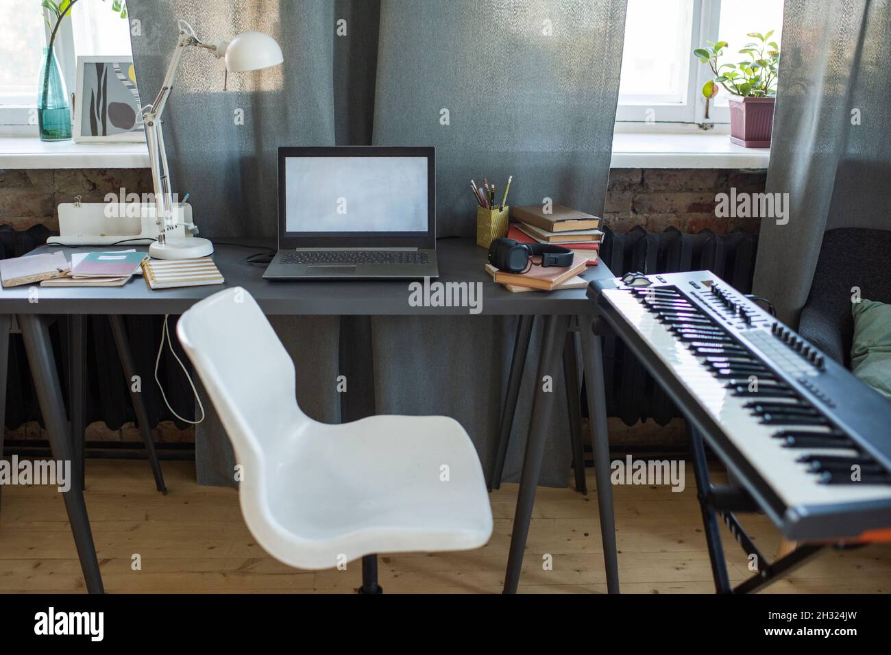 Chaise blanche de l'étudiant debout entre la table avec ordinateur portable et clavier de piano dans le milieu de la maison Banque D'Images