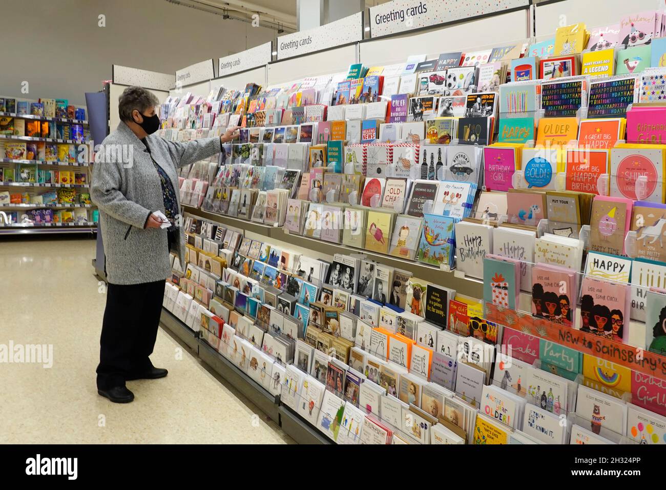 Femme mature senior magasiner dans un supermarché Sainsburys allée naviguer pour sélectionner un message sur un rack de cartes de vœux coloré Angleterre Royaume-Uni Banque D'Images