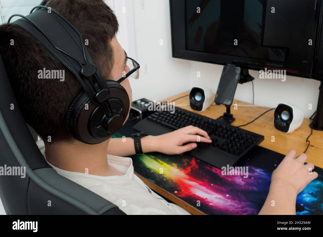 Un jeune joueur avec des écouteurs garçon jouant à un jeu d'ordinateur sur un ordinateur de bureau puissant modèle Release disponible Banque D'Images