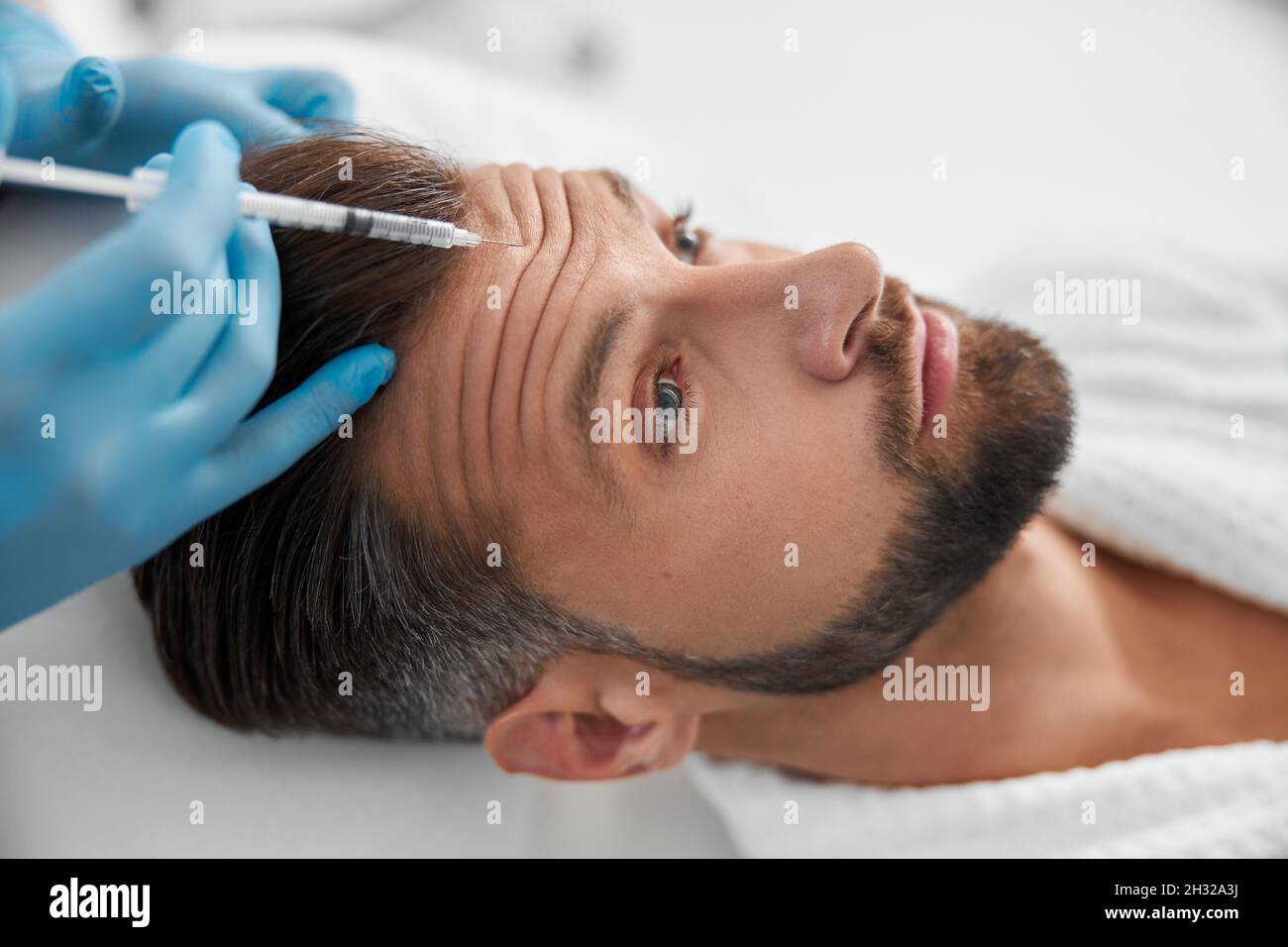 Médecin cosmétologue fait l'injection de l'enduit de levage dans le front ridé de l'homme mature en clinique Banque D'Images