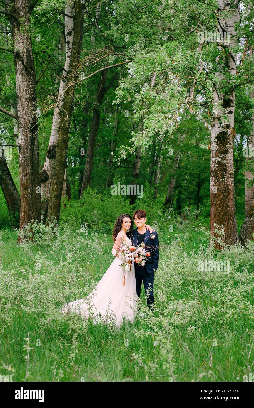 Jour de mariage.Jeunes jeunes mariés heureux dans une forêt verte fraîche.Portrait de la mariée et du marié.Mariage de printemps.Couple international.Cérémonie de mariage à l'extérieur. Banque D'Images