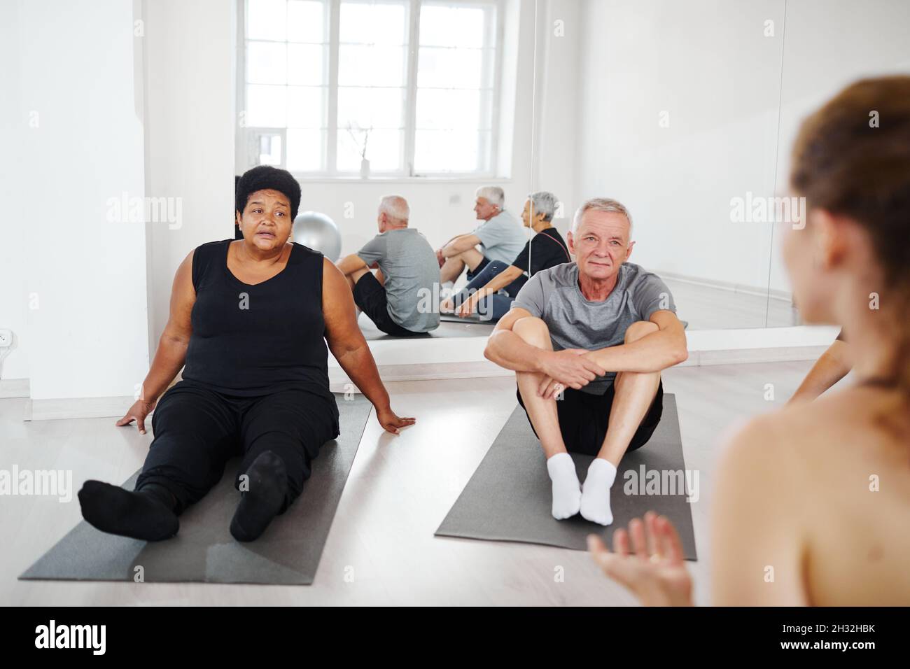 Personnes âgées effectuant des exercices de relaxation sur le sol et écoutant l'entraîneur pendant la gymnastique en studio Banque D'Images