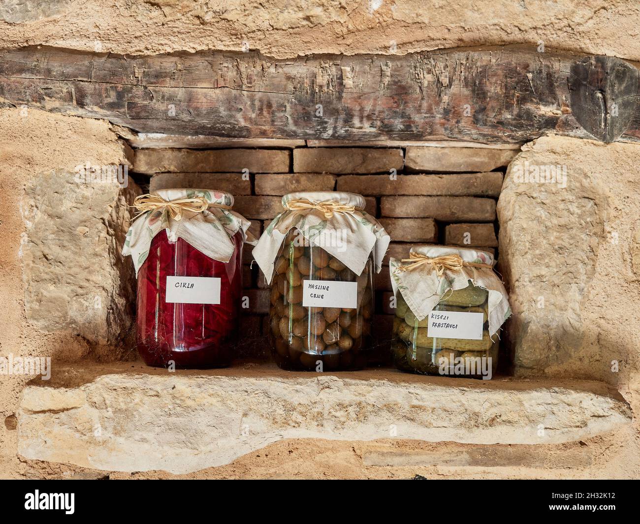 Variété de légumes en conserve: Betteraves concervées, olives marinées et concombres sur une étagère dans la cave d'une ancienne maison de village.Bocaux avec étiquettes et pro Banque D'Images