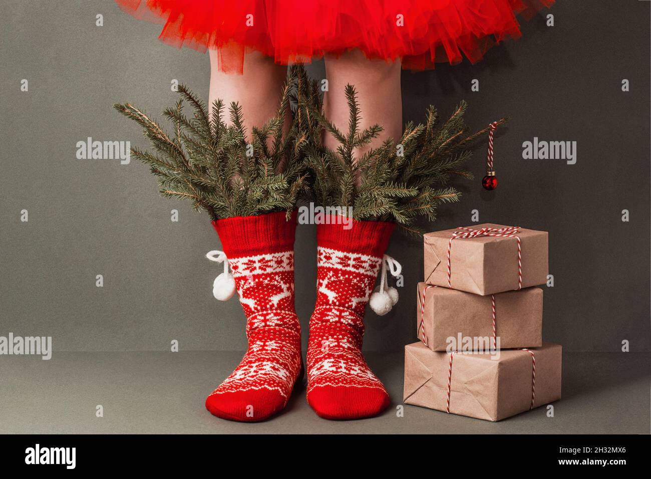 Jambes de femme en chaussettes rouges en laine avec ornements, branches de sapin et cadeaux de Noël sur fond vert.Joyeux Noël ou du nouvel an, cadeau créatif Banque D'Images