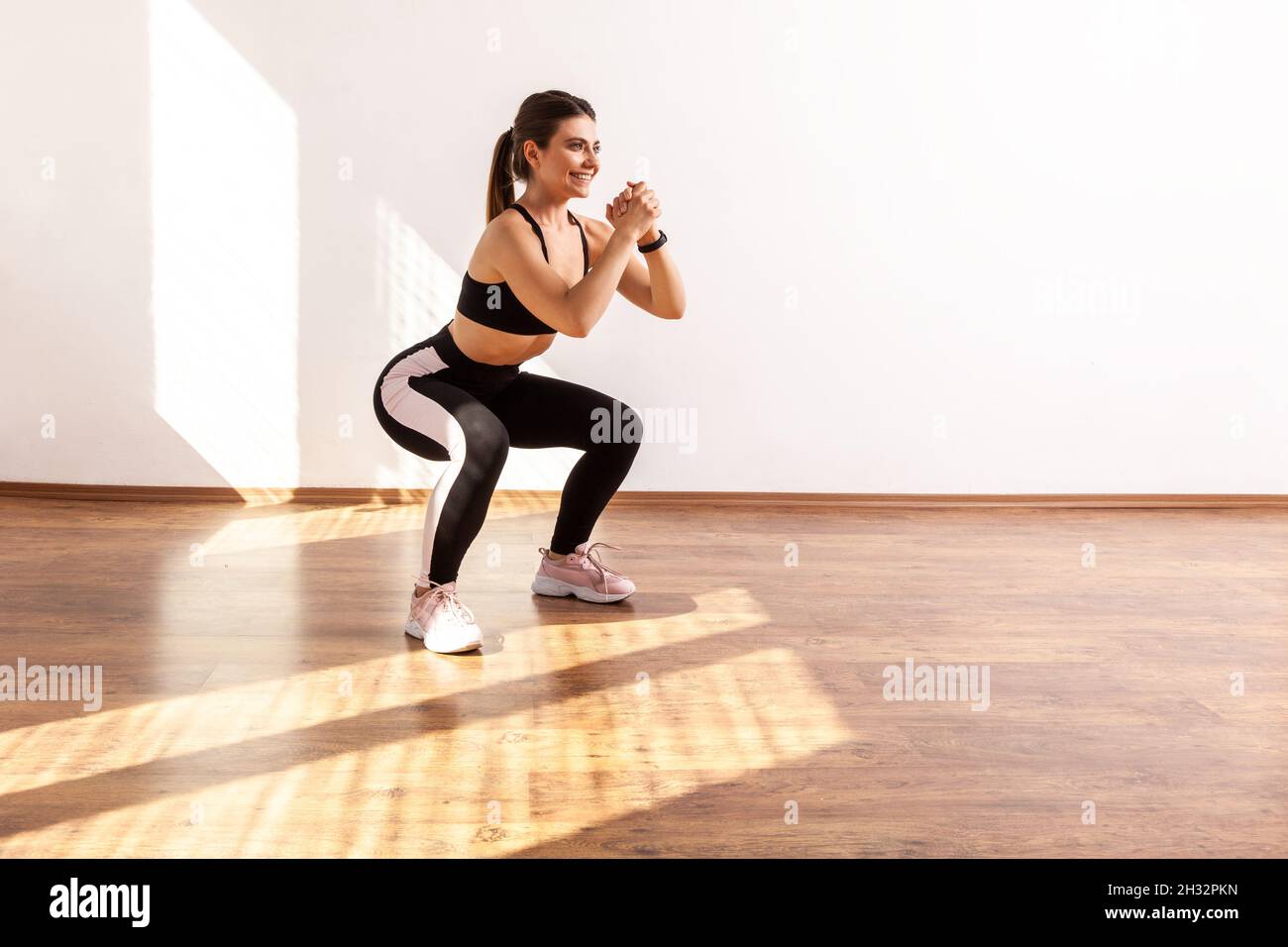 Profil d'une femme sportive qui fait du squat, exercice de sport du bas du  corps, échauffement et muscles d'entraînement, portant un haut de sport  noir et des collants.Prise de vue en studio