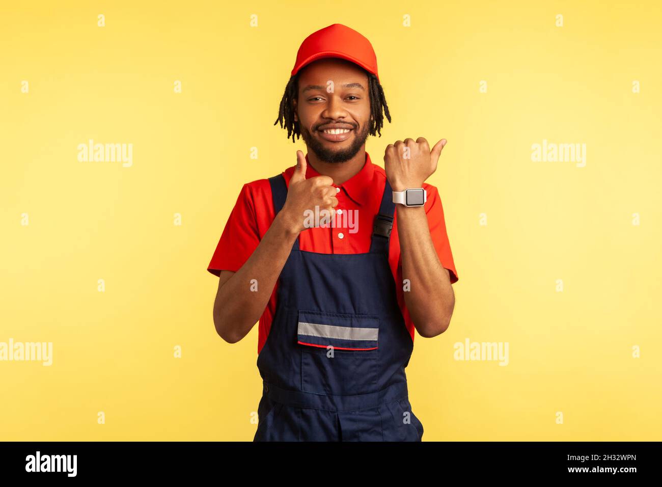 Homme de main ou constructeur positif montrant la montre intelligente sur sa main et le pouce vers le haut, comme le geste, satisfait avec un excellent service de livraison à temps.Studio d'intérieur isolé sur fond jaune. Banque D'Images