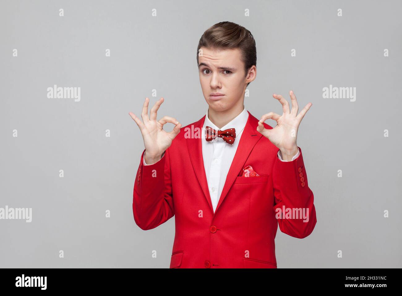 Je suis ok, approbation.Portrait de jeune gentleman tendance avec une coiffure élégante portant un smoking rouge et un noeud papillon montrant un geste de main correct, satisfait complètement d'accord. studio tourné isolé sur fond gris Banque D'Images