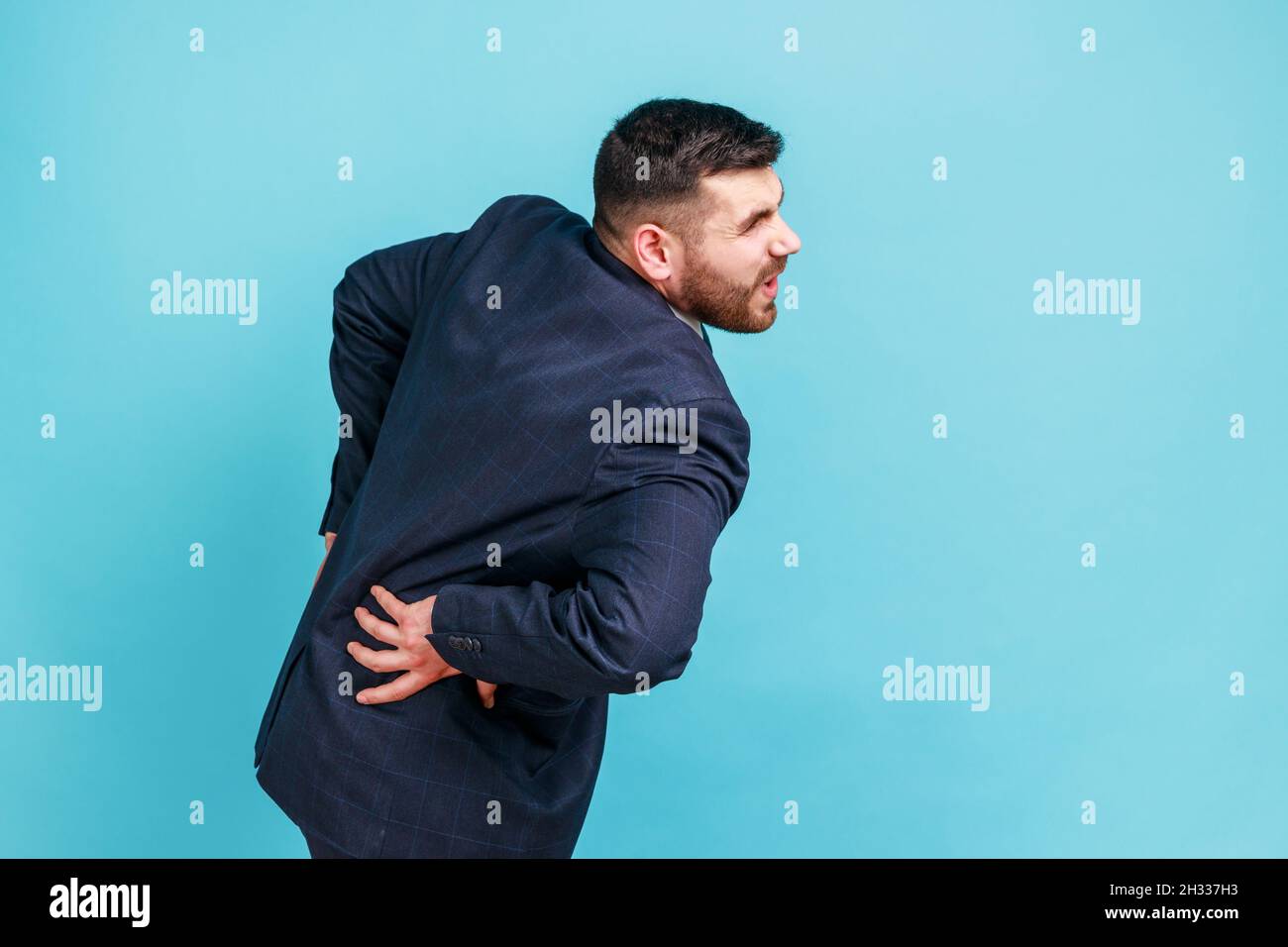 Problèmes de rachis.Jeune homme d'affaires adulte en costume de style officiel tenant son dos, ayant une douleur soudaine dans le bas du dos, nerf pincé ou inflammation rénale.Studio d'intérieur isolé sur fond bleu. Banque D'Images