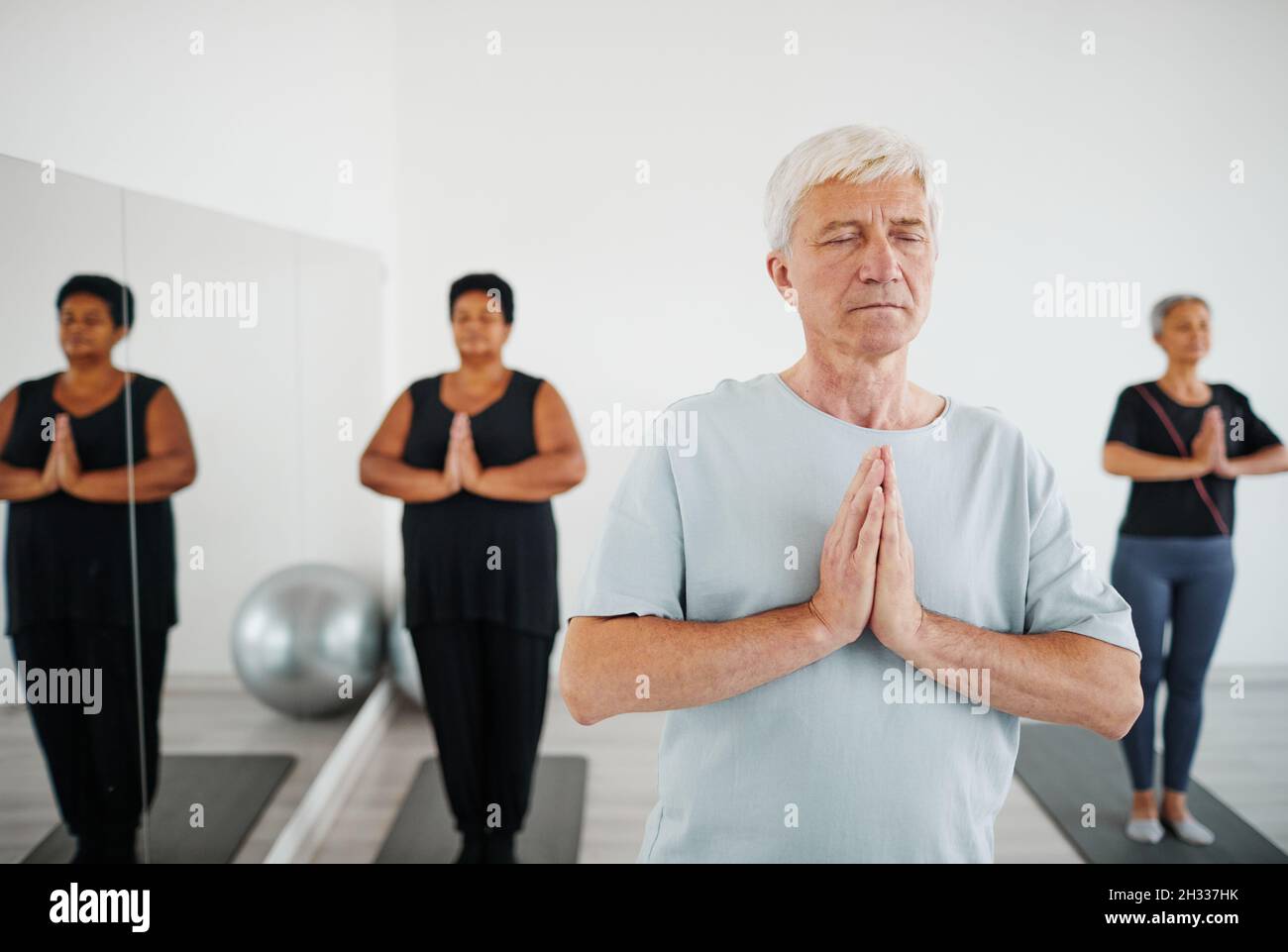 Portrait de l'homme âgé avec les yeux fermés pratiquant la méditation pendant la classe de yoga de groupe Banque D'Images