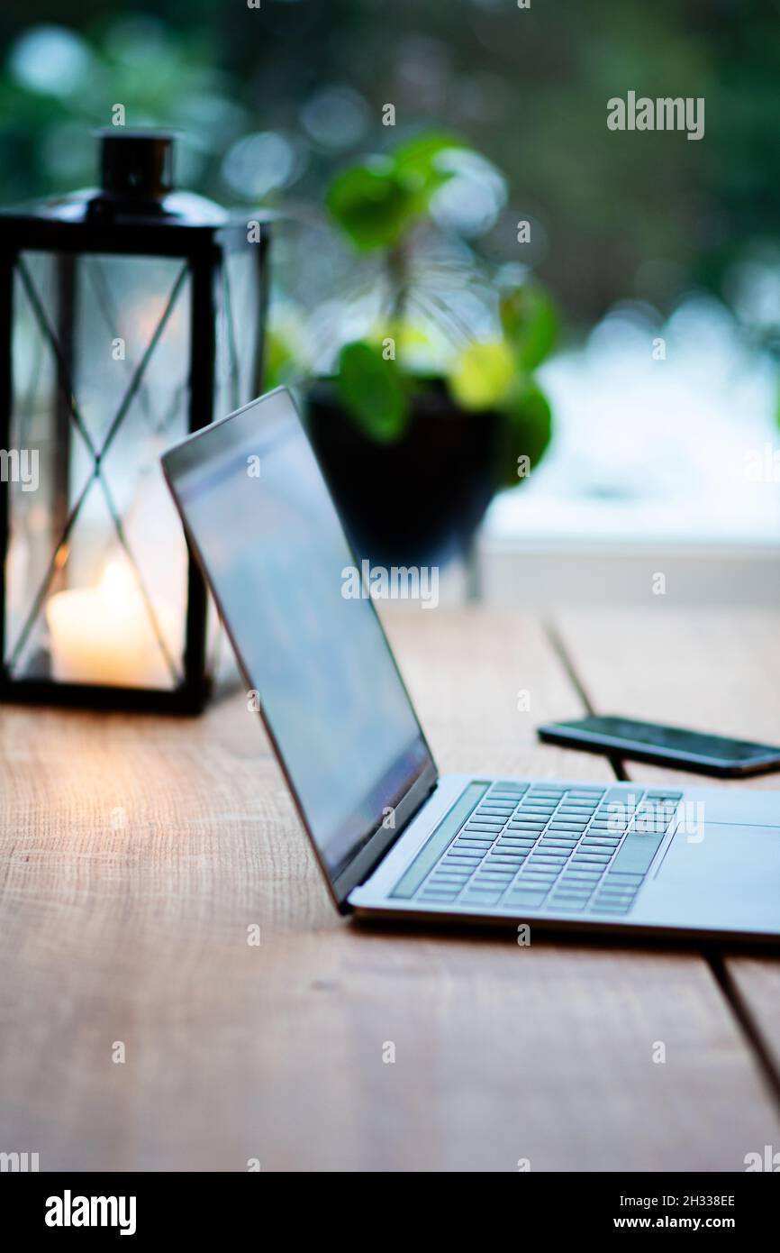 Travail à domicile avec ordinateur portable et mobile sur la table en bois.Sur la table se trouve également une lanterne de bougie pour créer une atmosphère confortable ce jour d'hiver. Banque D'Images