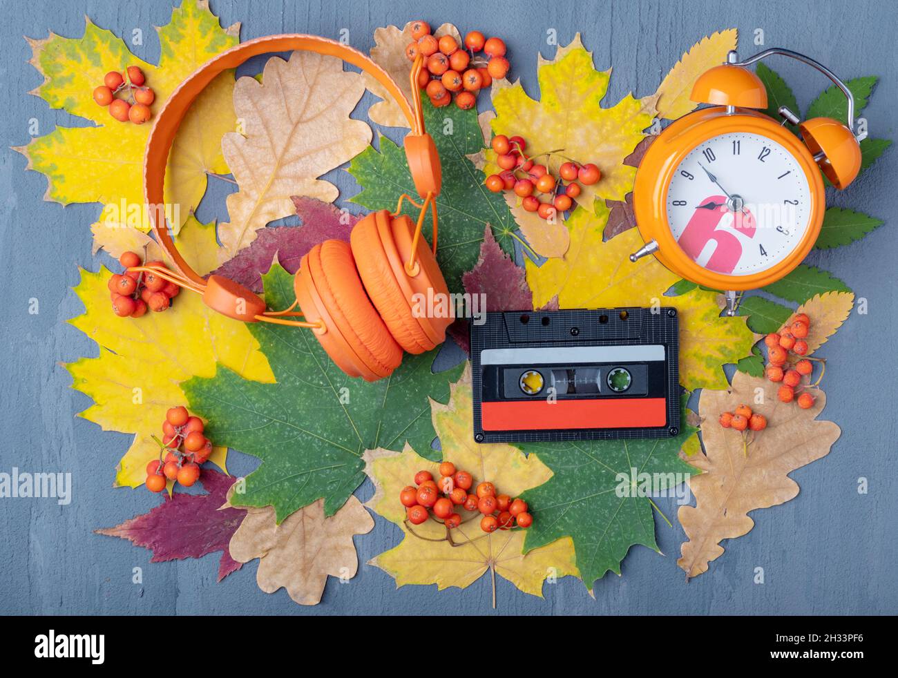 Un casque orange, un réveil et une cassette audio magnétique sur fond bleu avec des feuilles rouges et jaunes et des baies orange.favorit conceptuel Banque D'Images