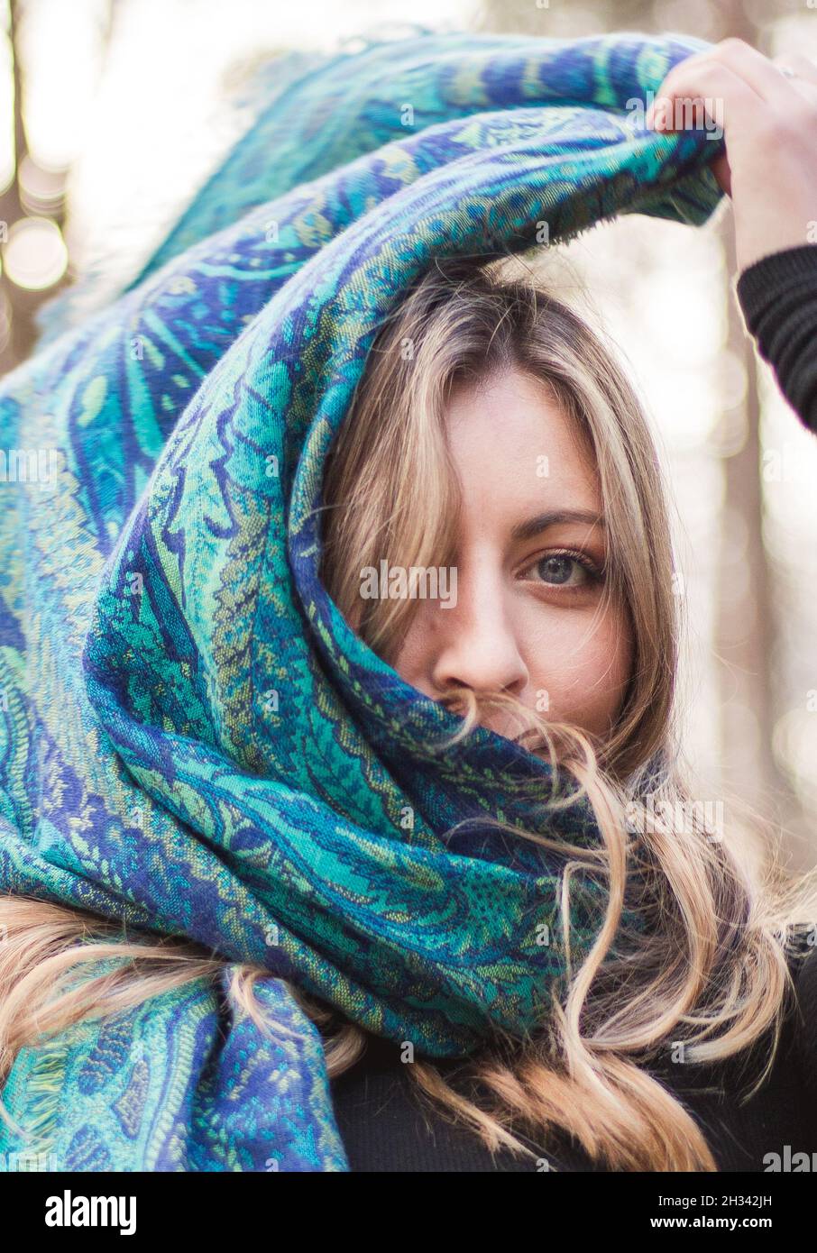 Jeune adulte blond aux yeux bleus et haut noir portant une écharpe bleue dans les bois Banque D'Images