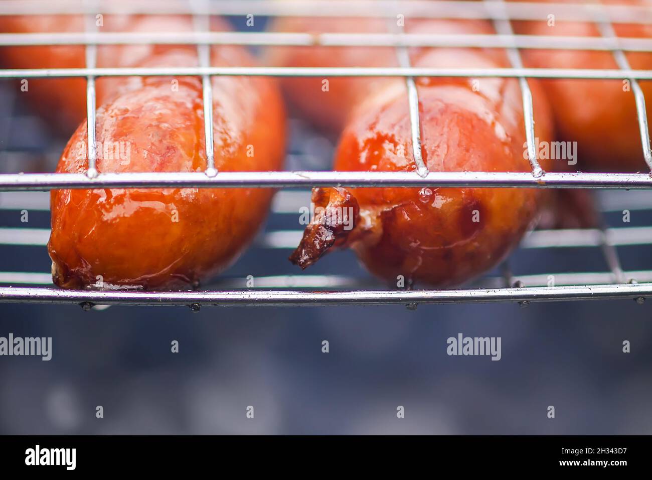 De savoureuses saucisses friture sur un brazier avec des charbons chauds en plein air à la campagne en été.Processus de cuisson.Barbecue. Banque D'Images