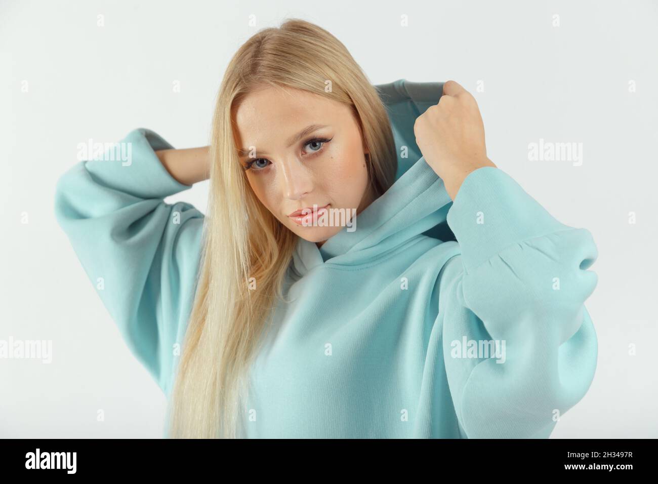 Jeune femme portant un sweat à capuche turquoise sur fond blanc.Look sportif décontracté pour femme Banque D'Images