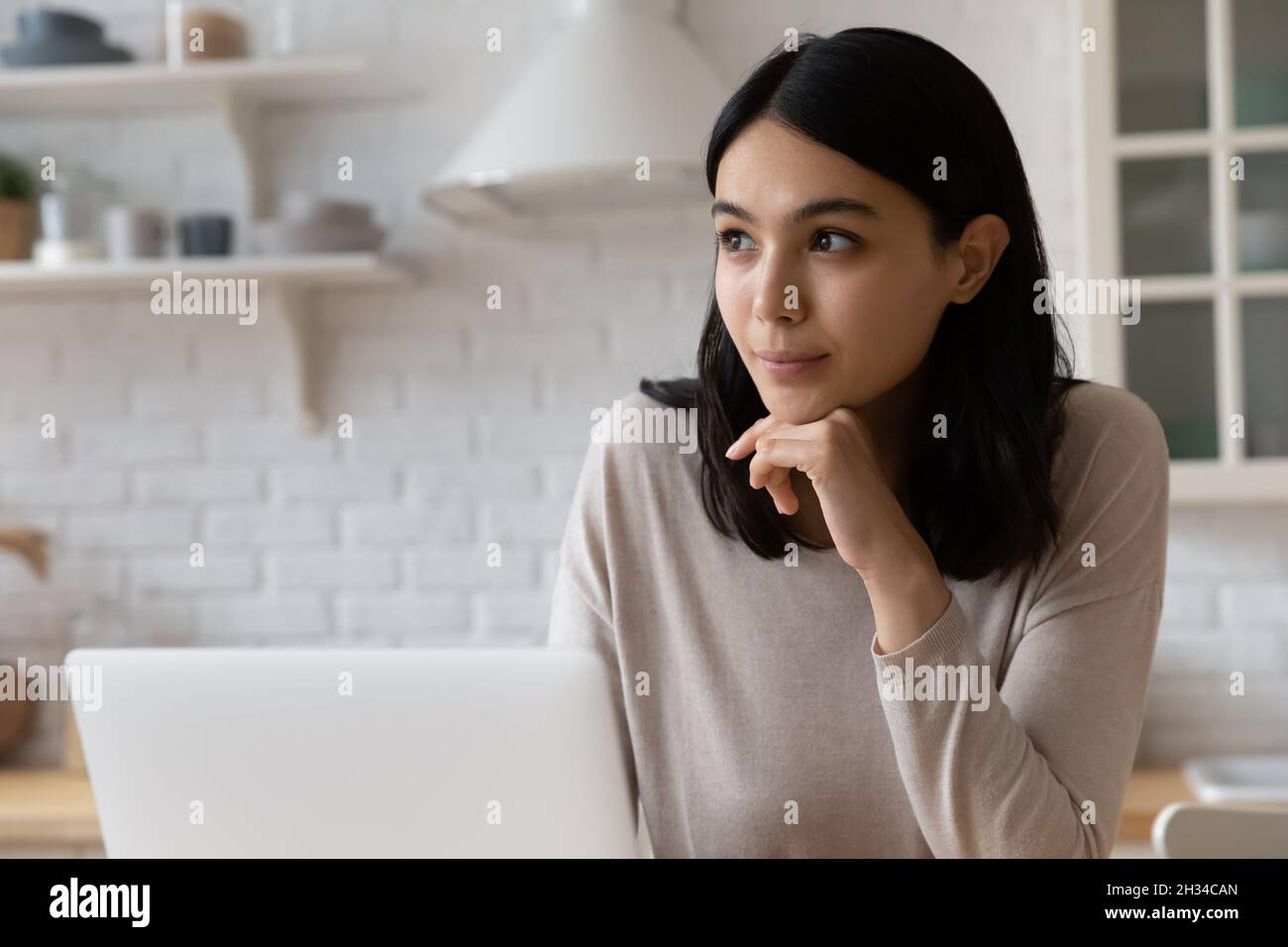 Bonne fille étudiante asiatique bien réfléchie assise sur un ordinateur portable Banque D'Images