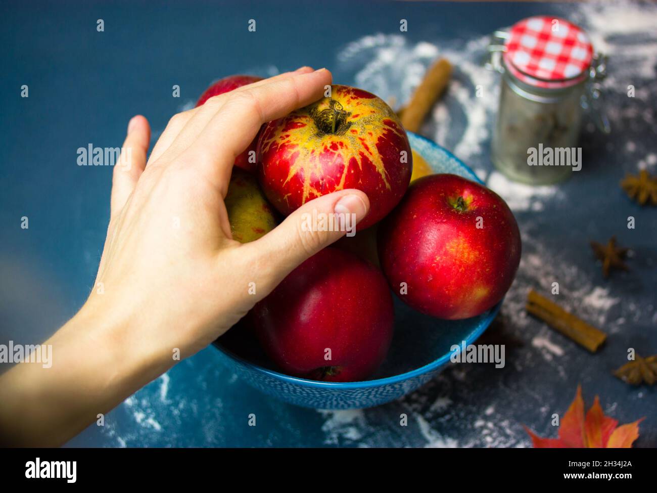 La main d'une femme atteint une pomme rouge mûre dans un bol. Choisir des fruits pour faire une tarte traditionnelle aux pommes de Thanksgiving. Ingrédients pour cuire à la maison Banque D'Images
