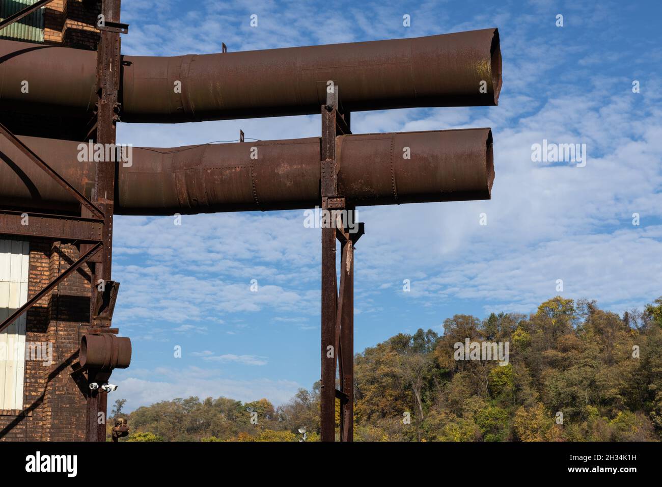 Deux grands tubes ouverts en métal tuyaux, très rouillés, montés sur le côté d'un bâtiment d'entrepôt, ciel bleu au-delà, aspect horizontal Banque D'Images