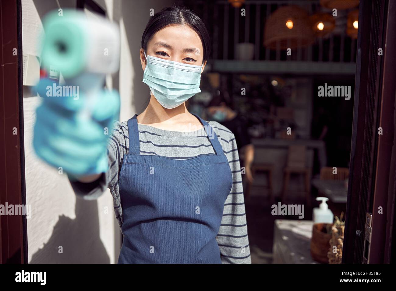 Serveuse tenant un thermomètre infrarouge à l'entrée du restaurant Banque D'Images
