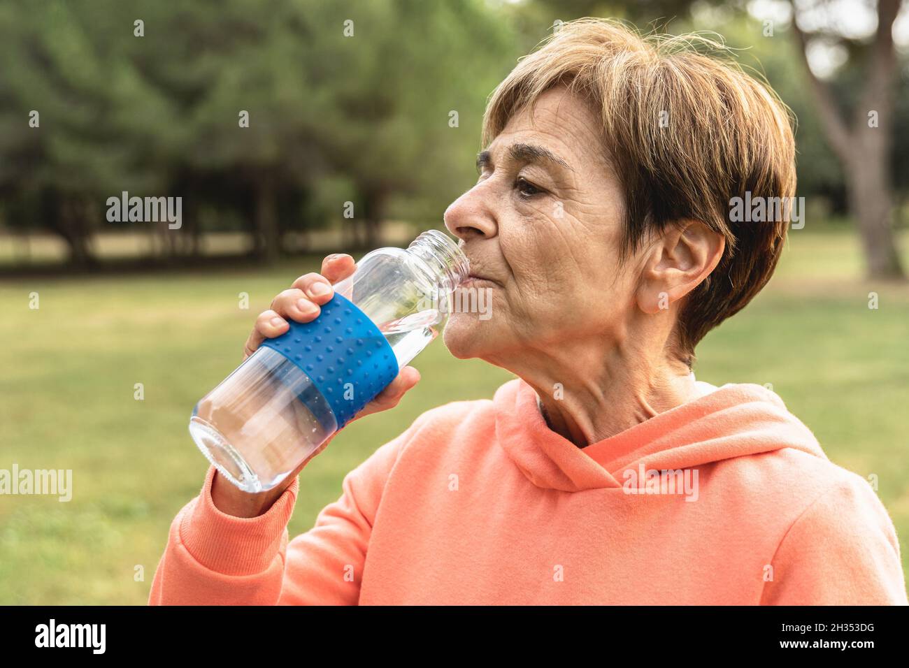 Femme âgée buvant de l'eau après une routine de jogging sportive en plein air dans le parc de la ville - exercice de personnes âgées et un mode de vie sain Banque D'Images