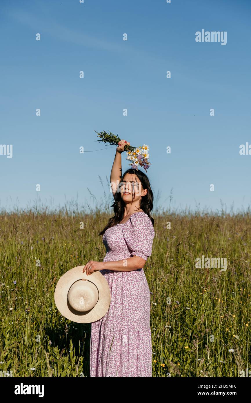 Portrait d'une belle jeune femme debout dans un champ ou un pré et tenant un bouquet de fleurs sauvages Banque D'Images