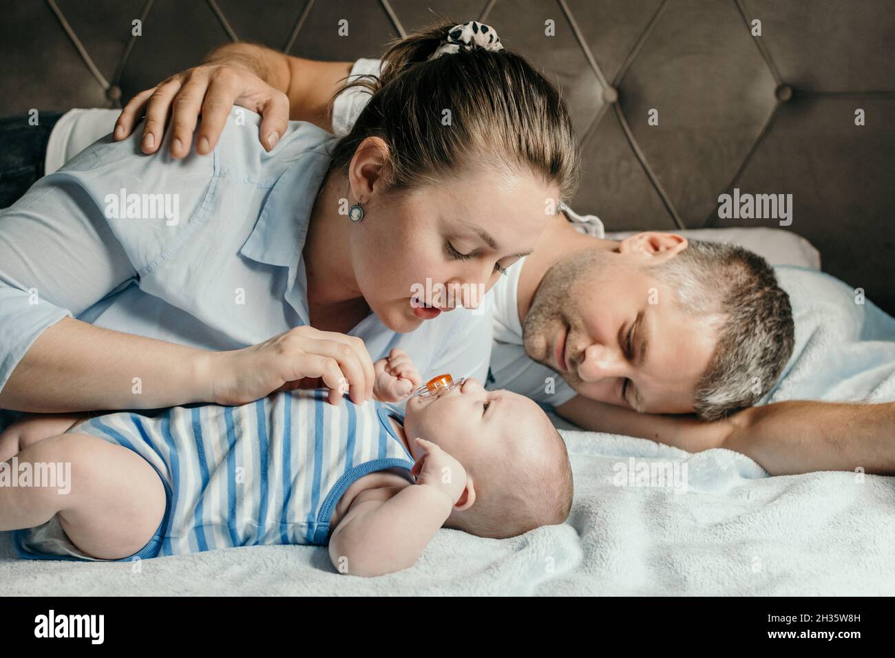 La mère et le père se couchant avec leur nouveau-né bébé garçon au lit Banque D'Images