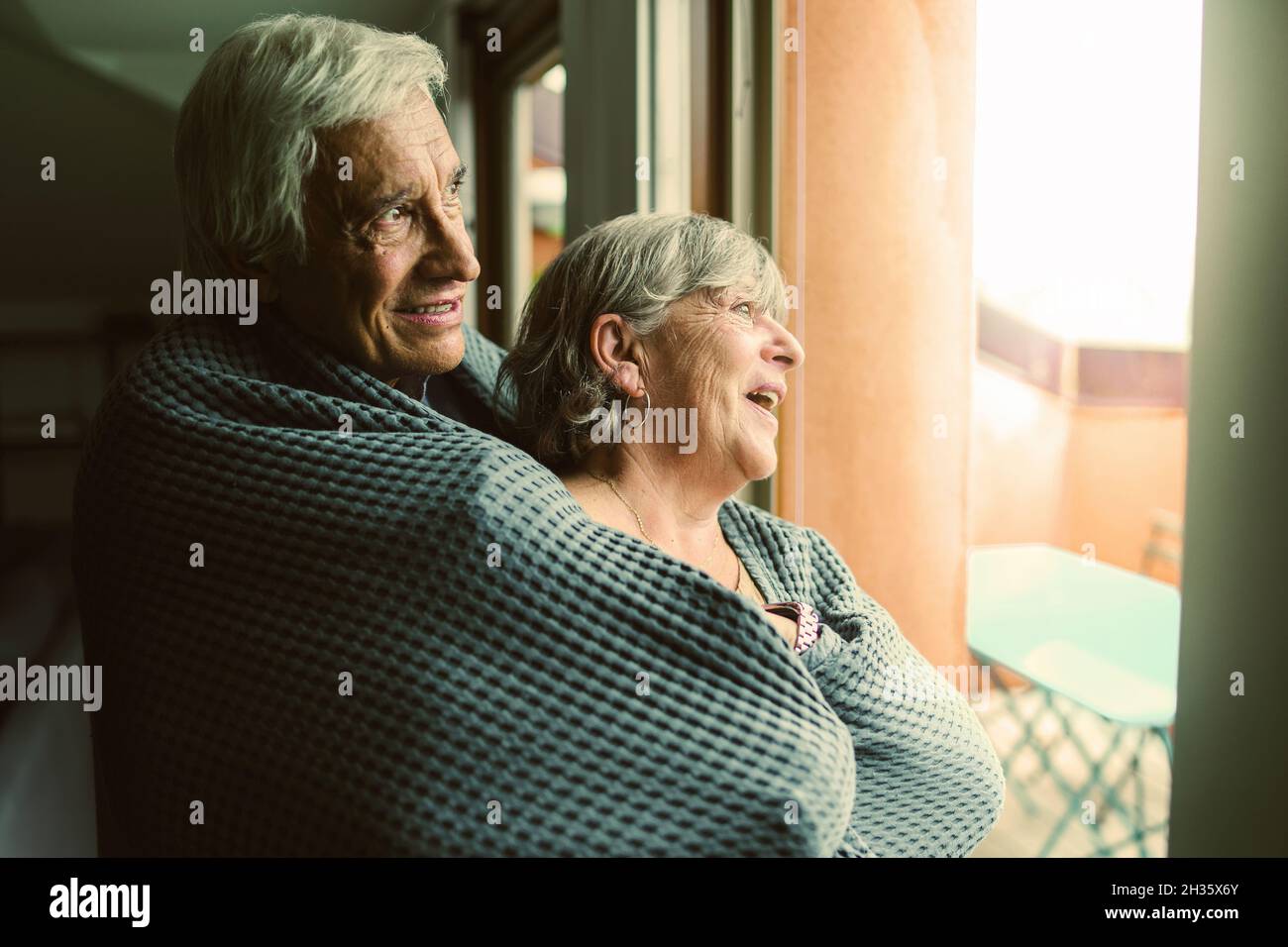 Couple de personnes âgées debout à la maison devant la fenêtre et regardant à l'extérieur - concept de couple de retraite romantique s'aimant l'un l'autre Banque D'Images
