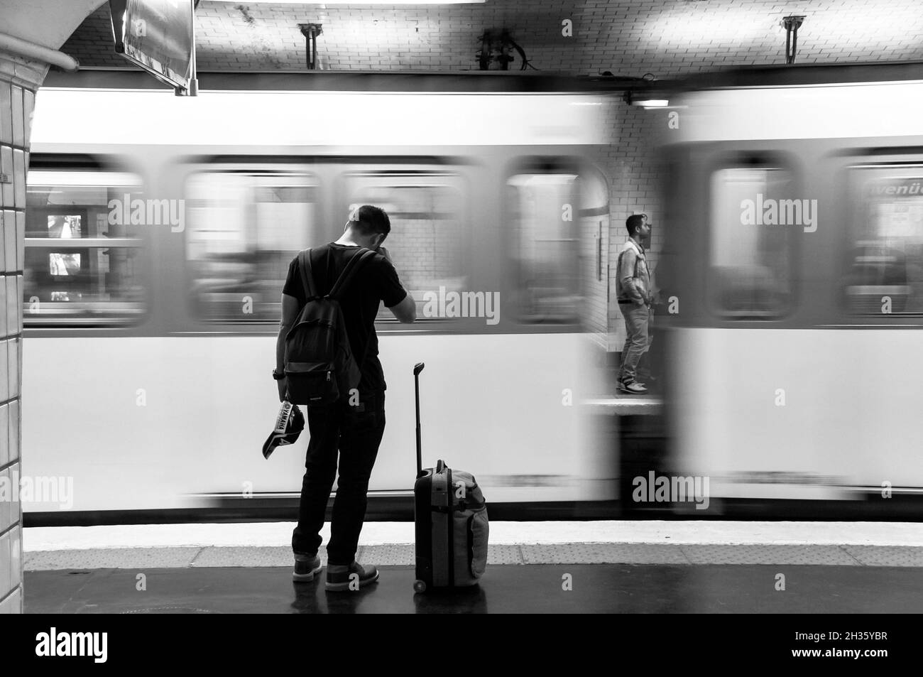 Paris (France) : atmosphère souterraine.Le voyageur a vu de l'arrière avec une valise le long d'une plate-forme dans une station de métro et train en mouvement Banque D'Images