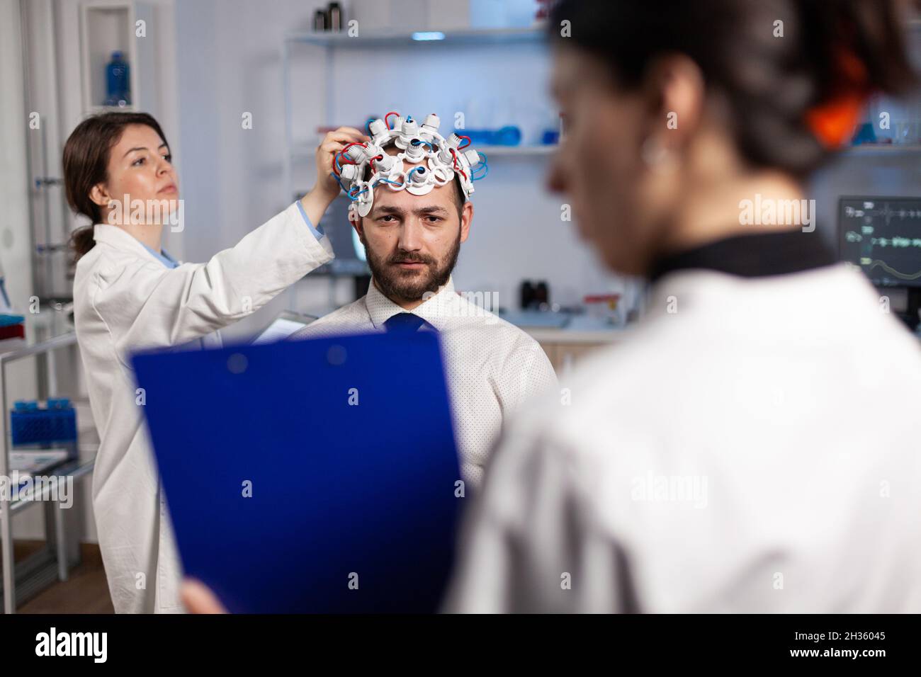 Neurologue spécialisé tenant le presse-papiers avec expliquer le traitement neurologique à l'homme patient tandis que la chercheuse femme ajustant le casque eeg.Médecin médecin médecin surveillant l'évolution de l'activité cérébrale Banque D'Images